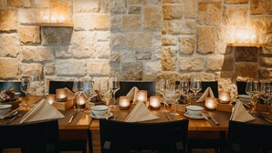 A dining table set with candles, glasses, and cutlery, against a stone wall backdrop.