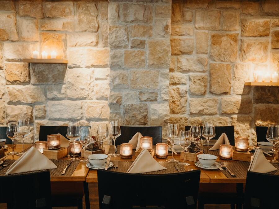 A dining table set with candles, glasses, and cutlery, against a stone wall backdrop.