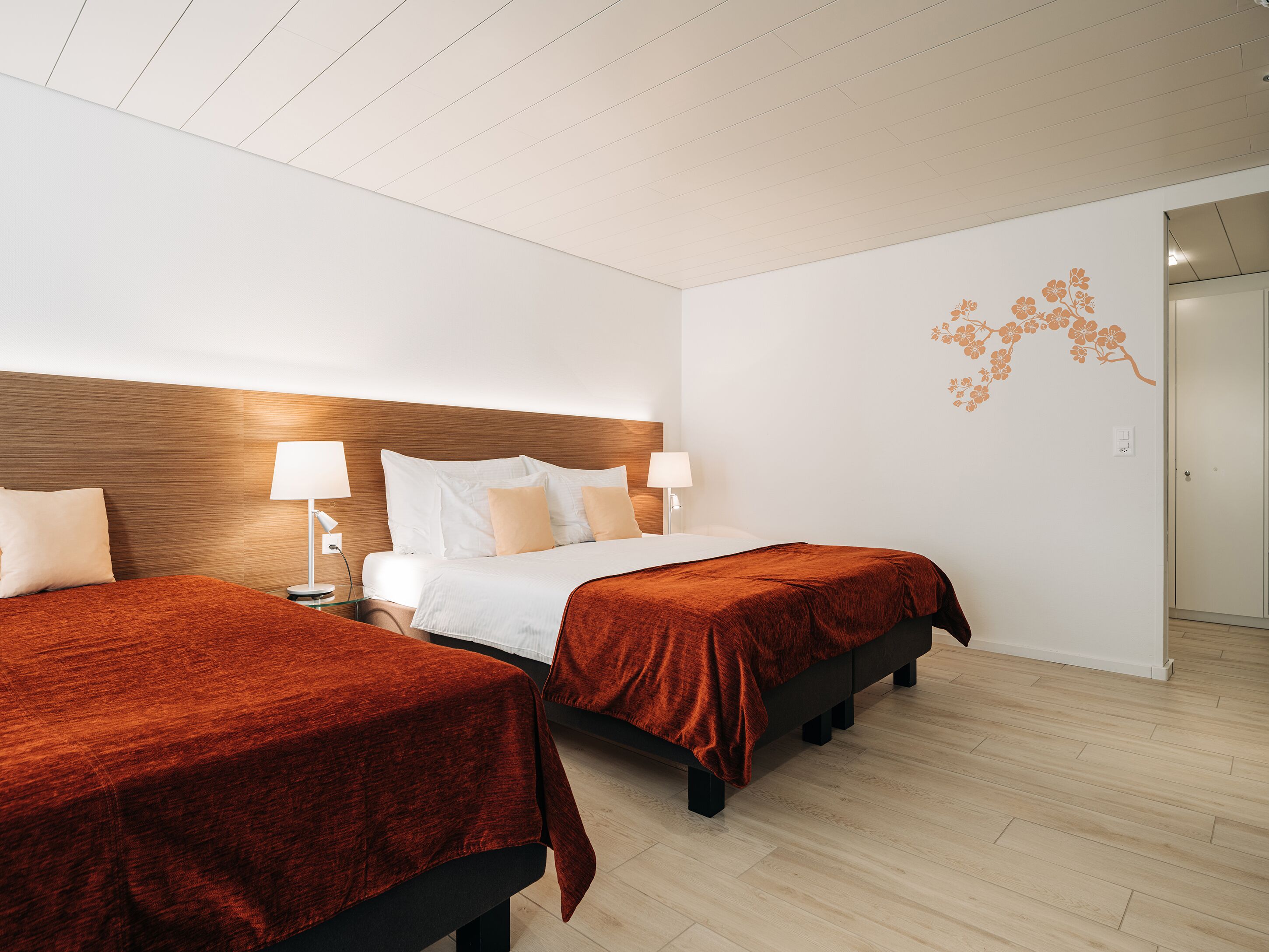A hotel room with two beds, wooden headboard, white walls, and a wooden floor.