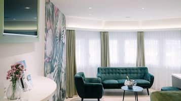 A modern living room with a green sofa, two armchairs, a round coffee table, and a white side table with a vase and glass.