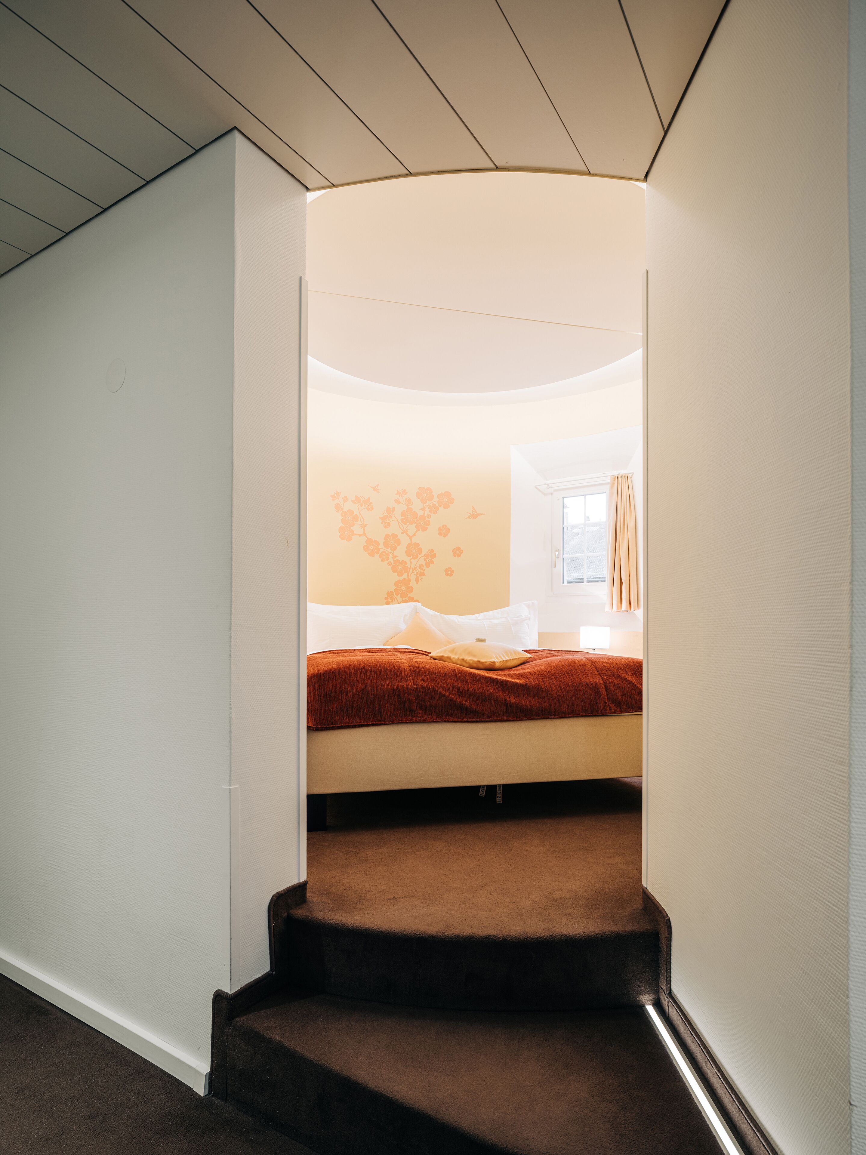 A bedroom with a bed, a window with curtains, and a wall with a floral design.