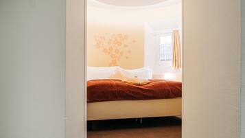 A bedroom with a bed, a window with curtains, and a wall with a floral design.