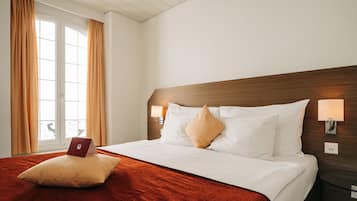 Une chambre d’hôtel avec un grand lit, deux lampes de chevet, une fenêtre avec des rideaux et une tête de lit en bois.