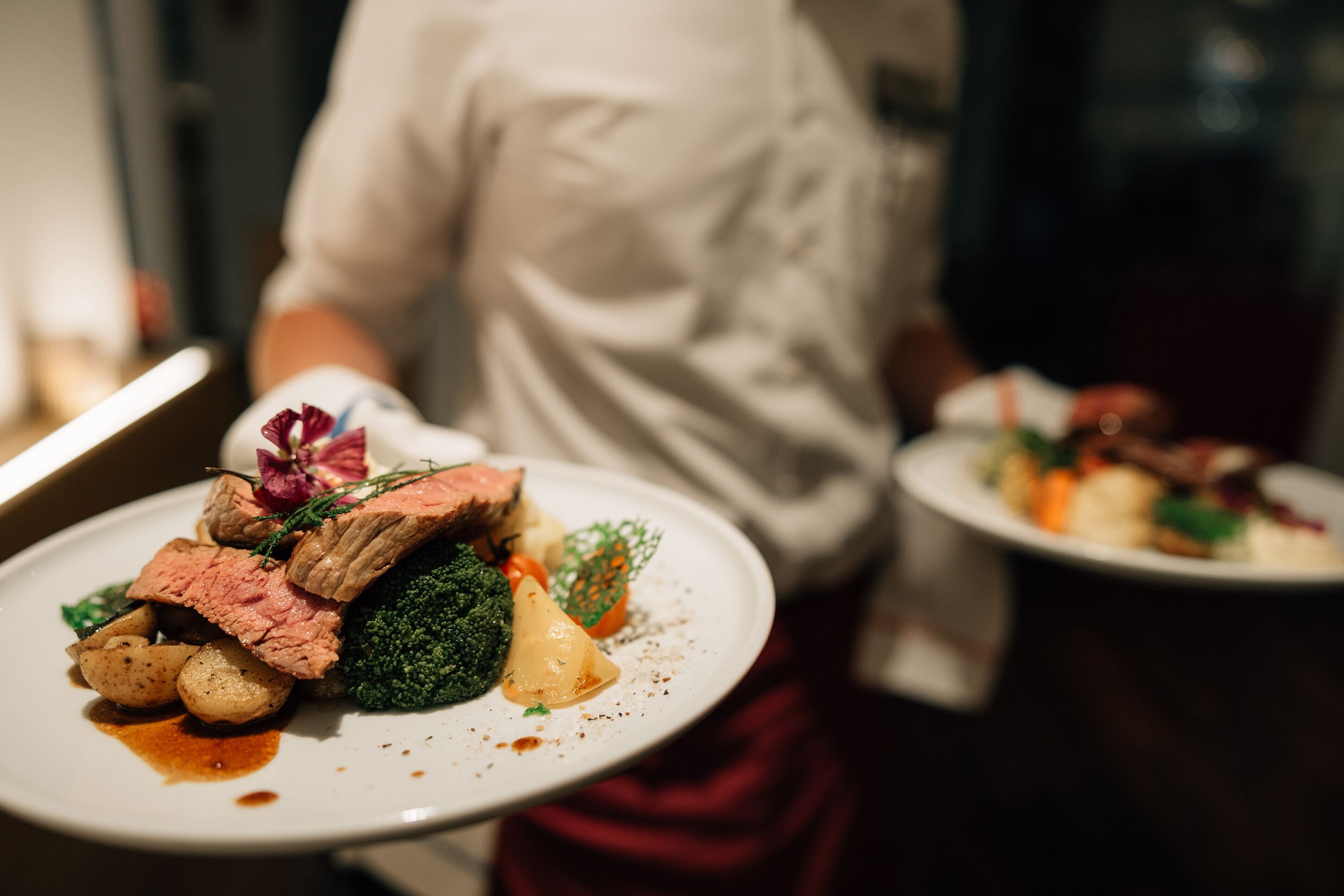 Un chef presenta un plato de comida con bistec, brócoli y patatas.