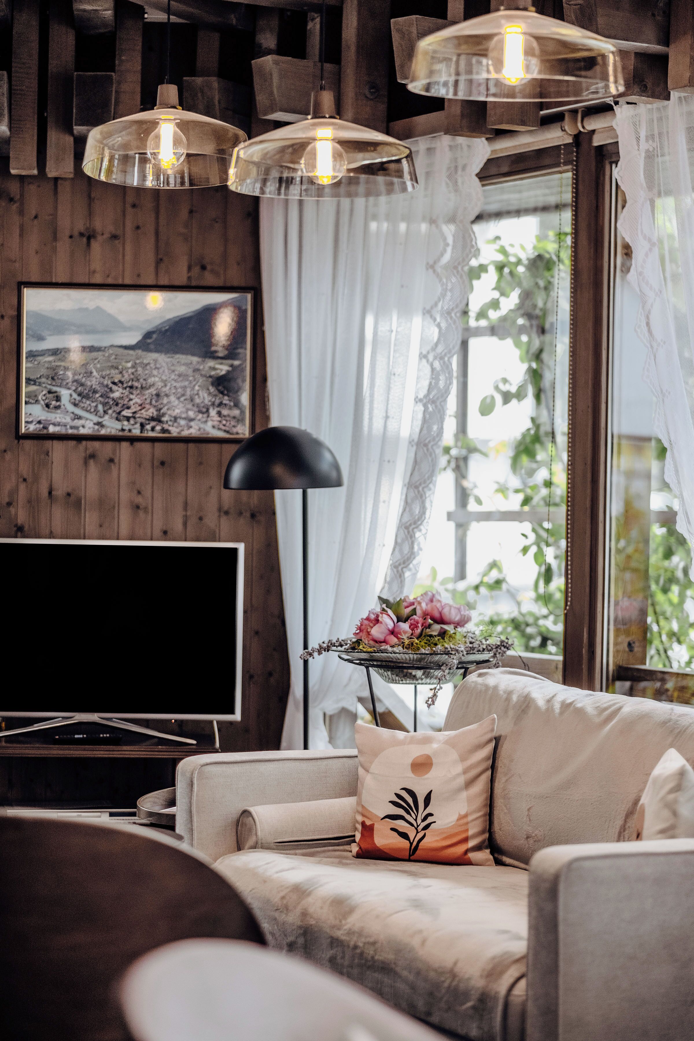 A cozy living room with a flat-screen TV, a sofa with decorative pillows, and a table with a floral arrangement.