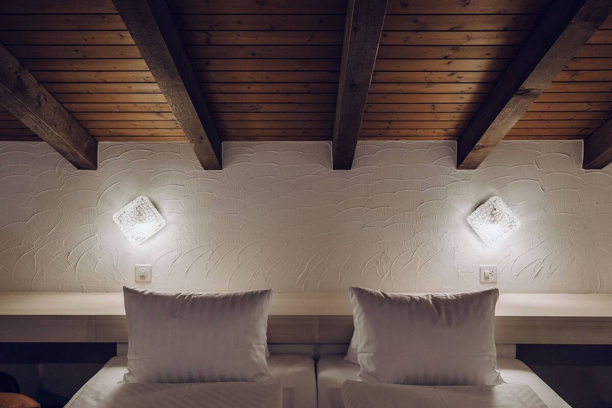 A room with a wooden ceiling, two bedside tables, and two wall-mounted lights.