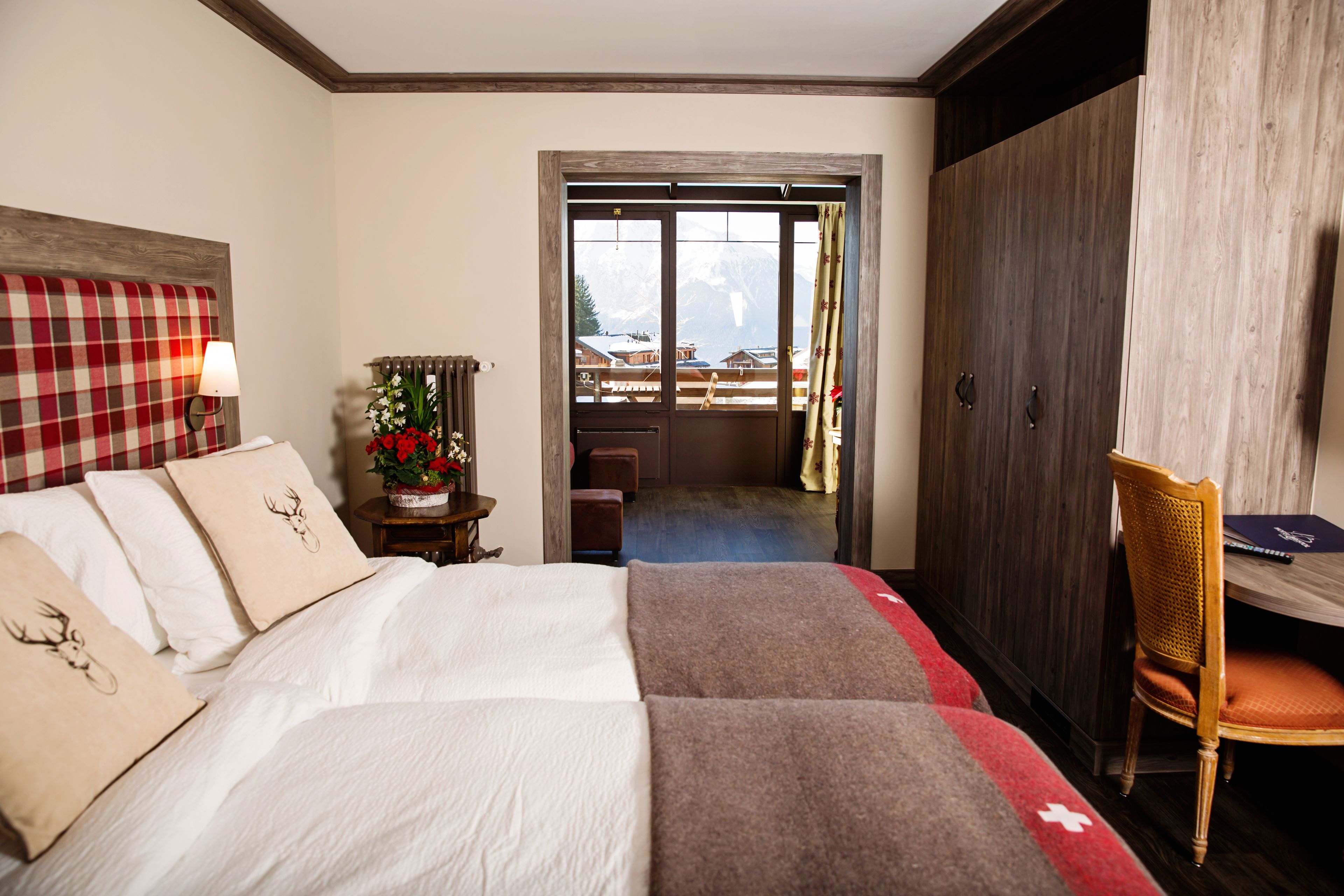 Habitación de hotel con cama, escritorio, silla y vista a las montañas a través de una puerta.