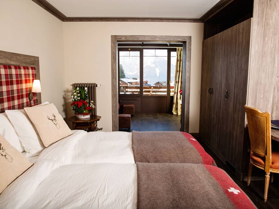 A hotel room with a bed, a desk, a chair, and a view of mountains through a door.