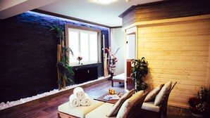 A spa area with a wooden bench, a massage table, and a window with a view of a stone wall and plants. - Hotel Bristol (Bagnes)