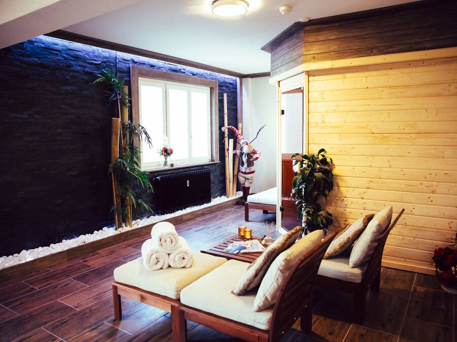 Un área de spa con un banco de madera, una camilla de masaje y un ventanal con vista a un muro de piedra y plantas.