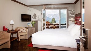 A hotel room with a bed, a desk, a chair, a TV, and a balcony with a mountain view. - Hotel Bristol (Bagnes)