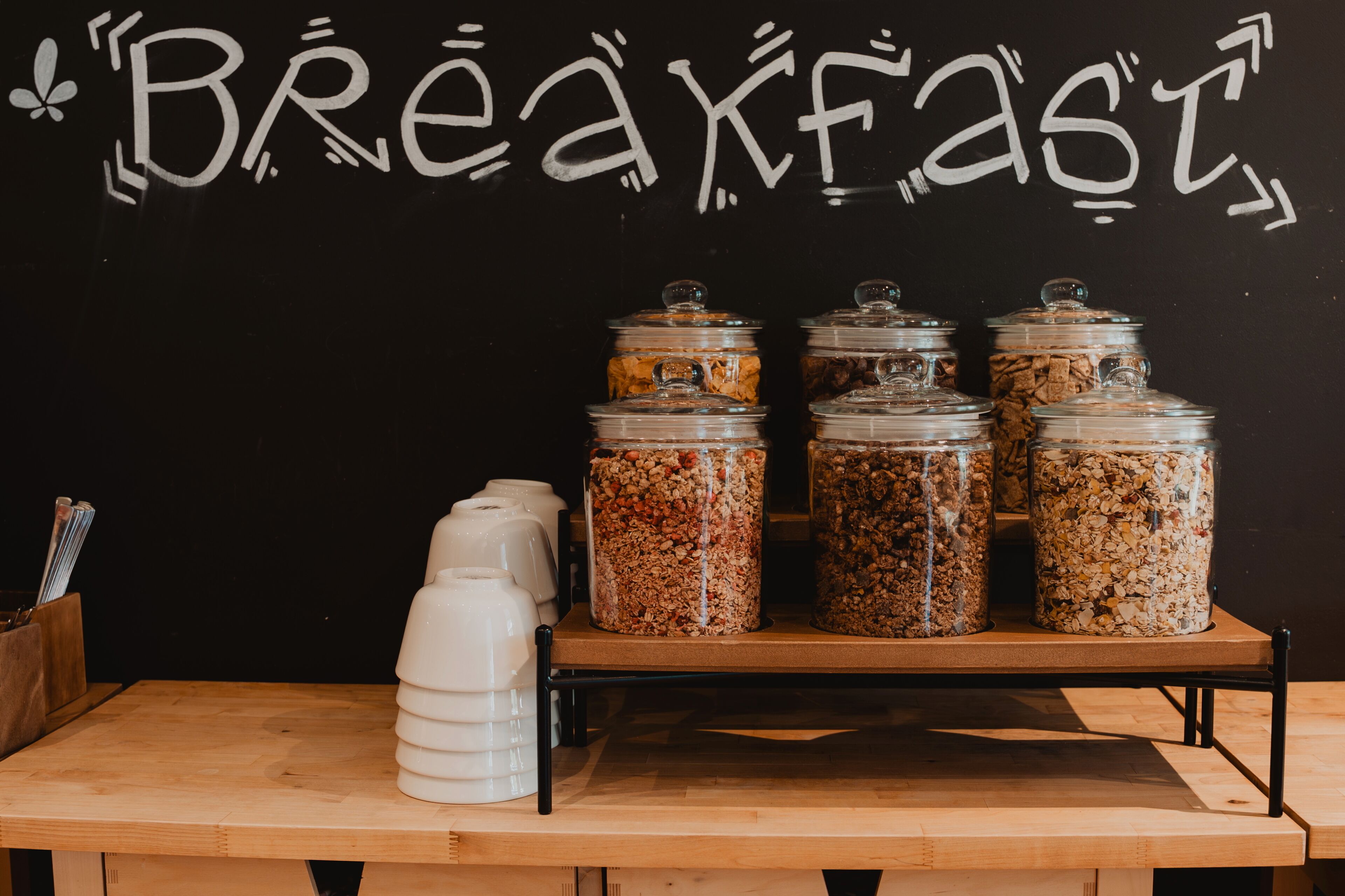 Una barra de desayuno con tarros de granola y un dispensador de leche.