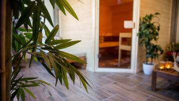A room with a wooden floor, a bed, a potted plant, and a table with candles.