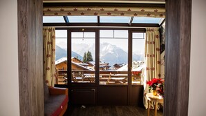 A cozy room with a wooden floor, a sofa, a table with a vase of flowers, and a view of mountains through large windows. - Hotel Bristol (Bagnes)