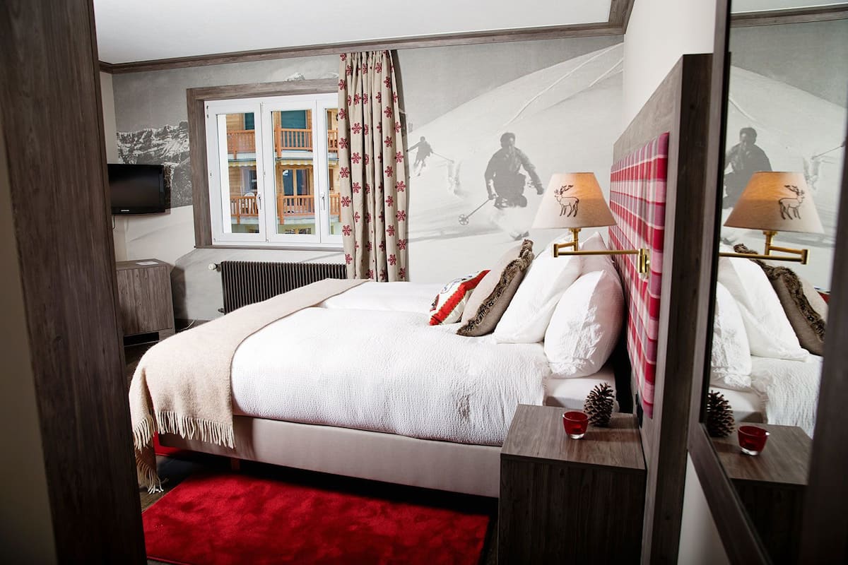 A bedroom with a bed, a red carpet, a window with curtains, a radiator, and a television on the wall.