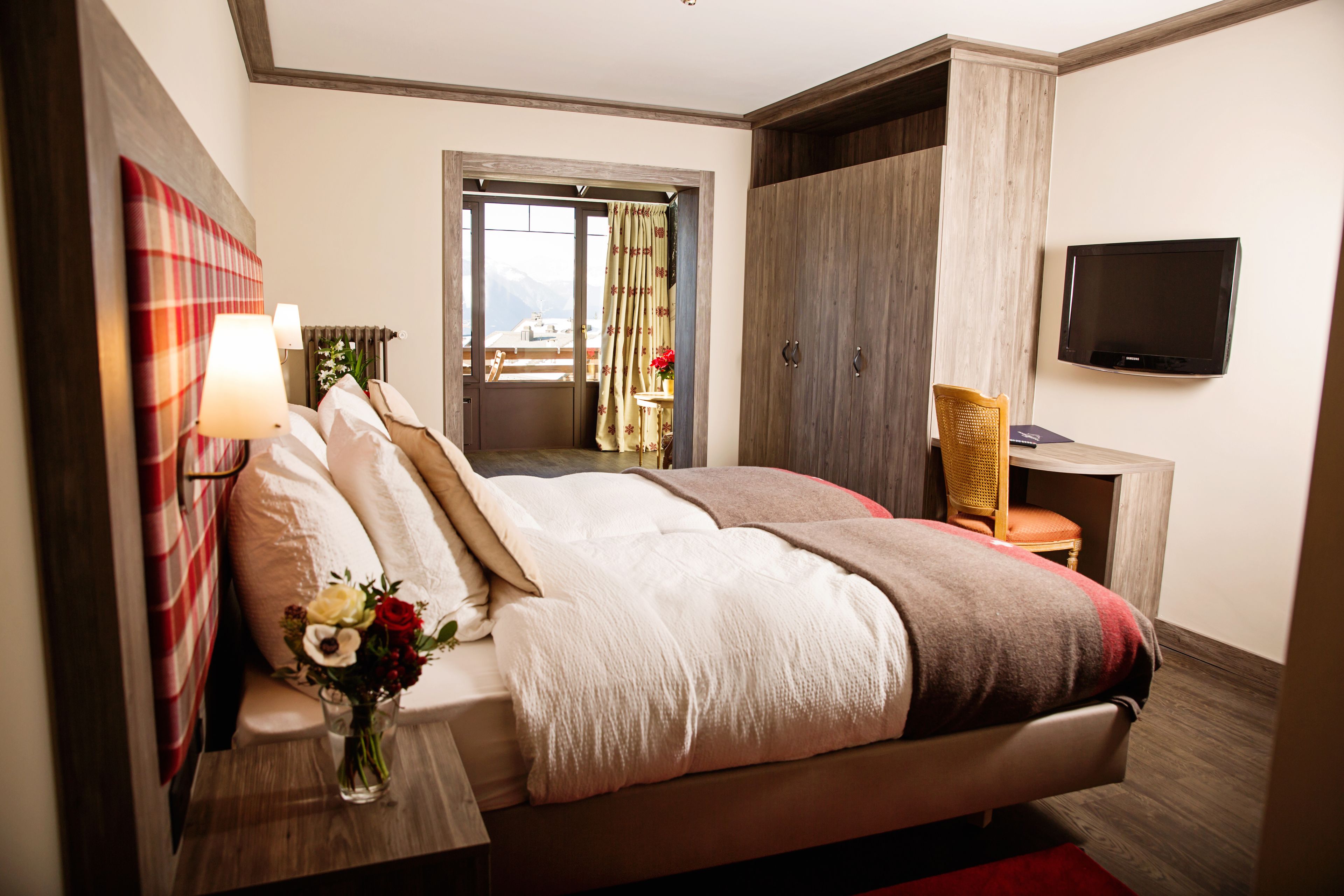 Hotelkamer met een groot bed, een televisie, een bureau met stoel en uitzicht op de bergen.