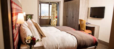 Habitación de hotel con una cama grande, televisión, escritorio con silla y vistas a la montaña a través de la ventana.