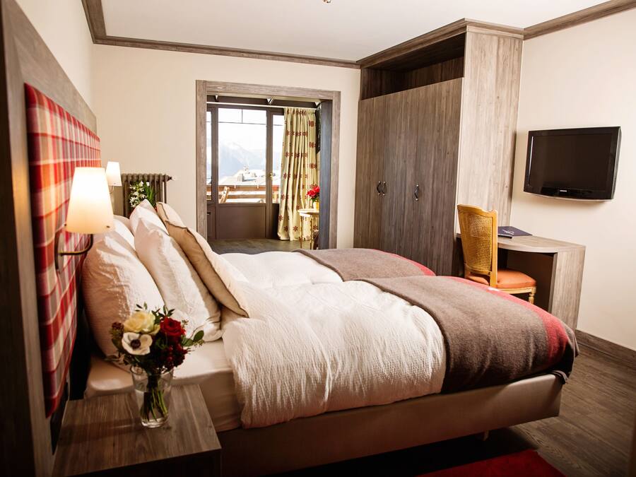 Hotelkamer met een groot bed, een televisie, een bureau met stoel en uitzicht op de bergen.