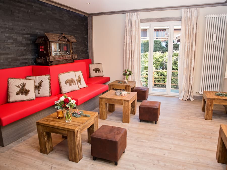 Una sala moderna con un sofá rojo, mesas de centro de madera y vistas a la vegetación a través de amplios ventanales.