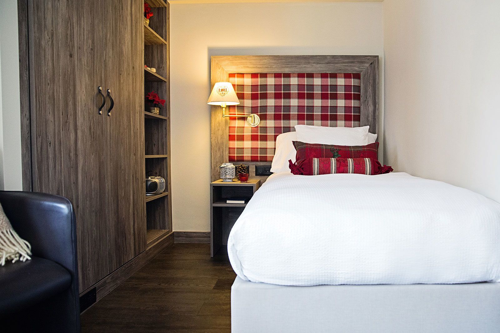 A hotel room with a bed, a nightstand, a lamp, a wardrobe, and a chair.