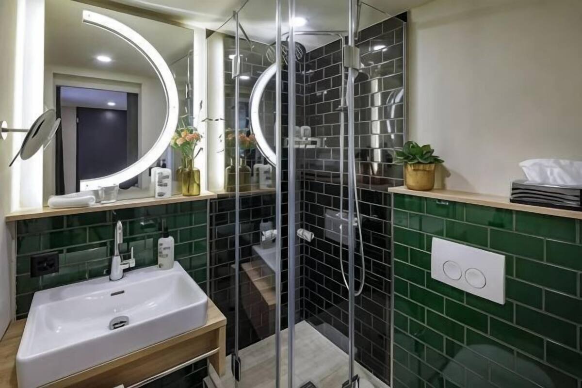 A bathroom with a glass-enclosed shower, a sink with a mirror, and a green tiled wall.