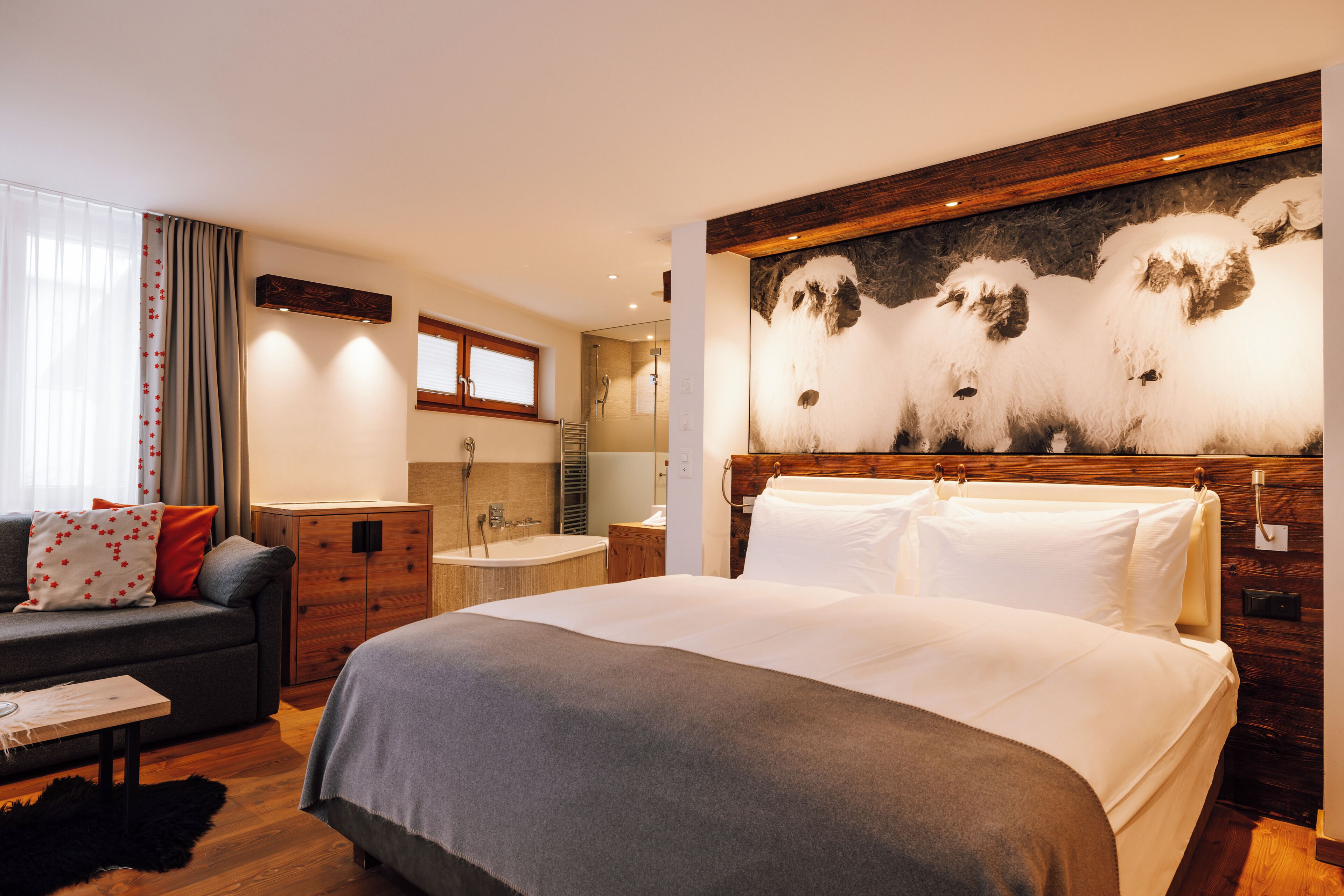 Una habitación de hotel moderna con una cama grande, un sofá, un cabecero de madera, un cuadro y un baño con bañera y ducha.