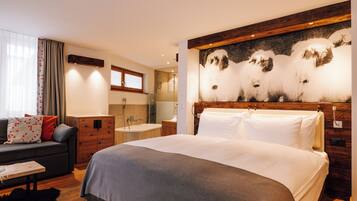 Una habitación de hotel moderna con una cama grande, un sofá, un cabecero de madera, un cuadro y un baño con bañera y ducha.