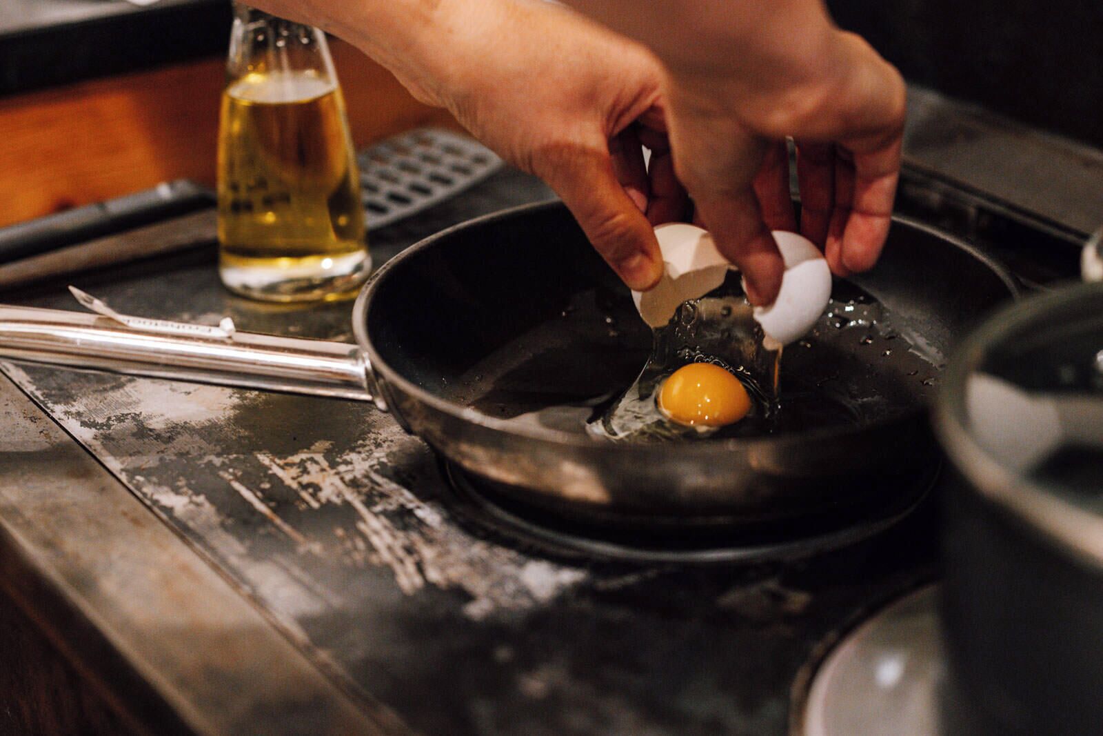 A hand cracking an egg into a frying pan on a stove.