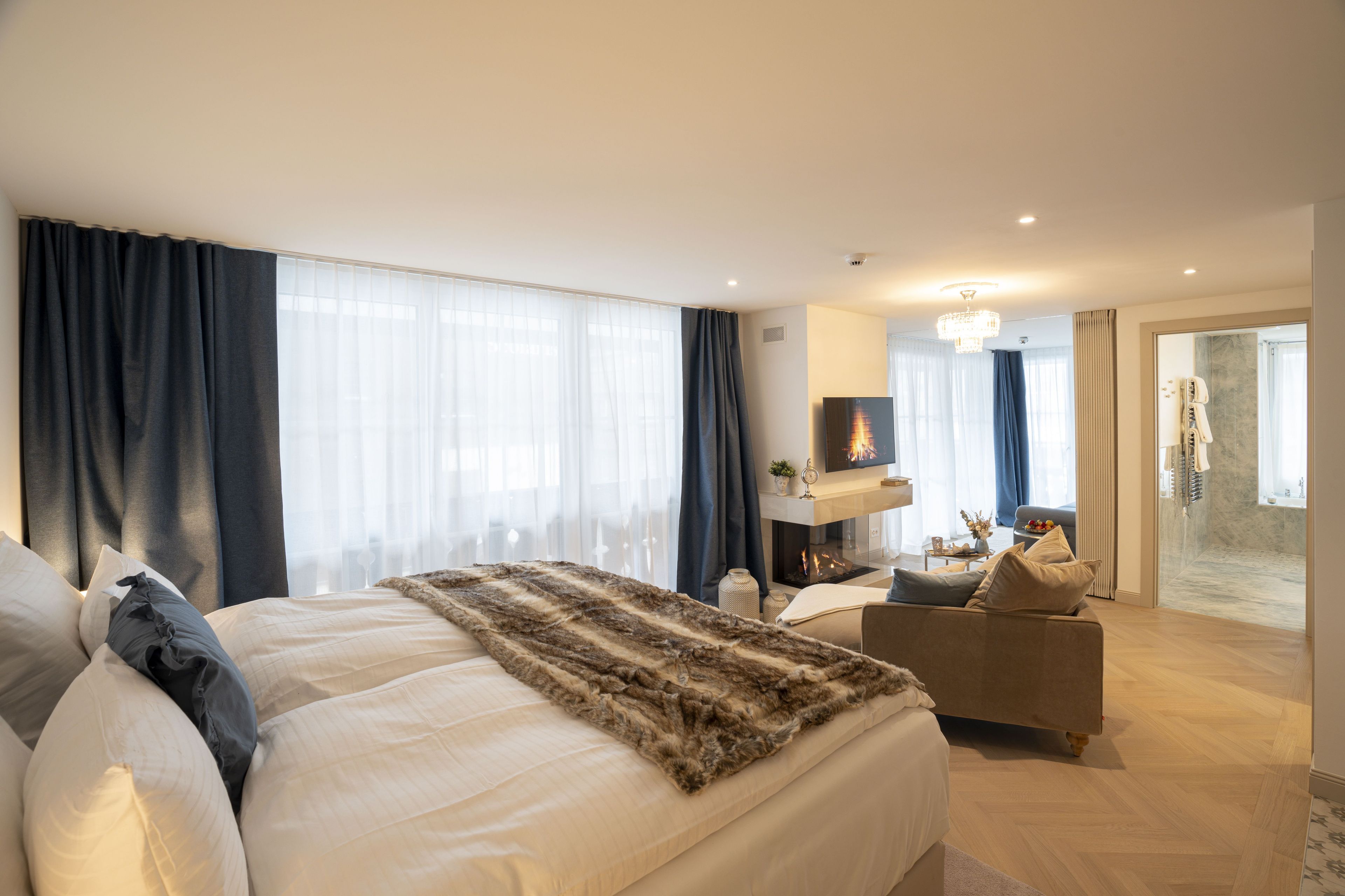 Una habitación de hotel moderna con una cama grande, un sofá, una chimenea y vistas de la ciudad.