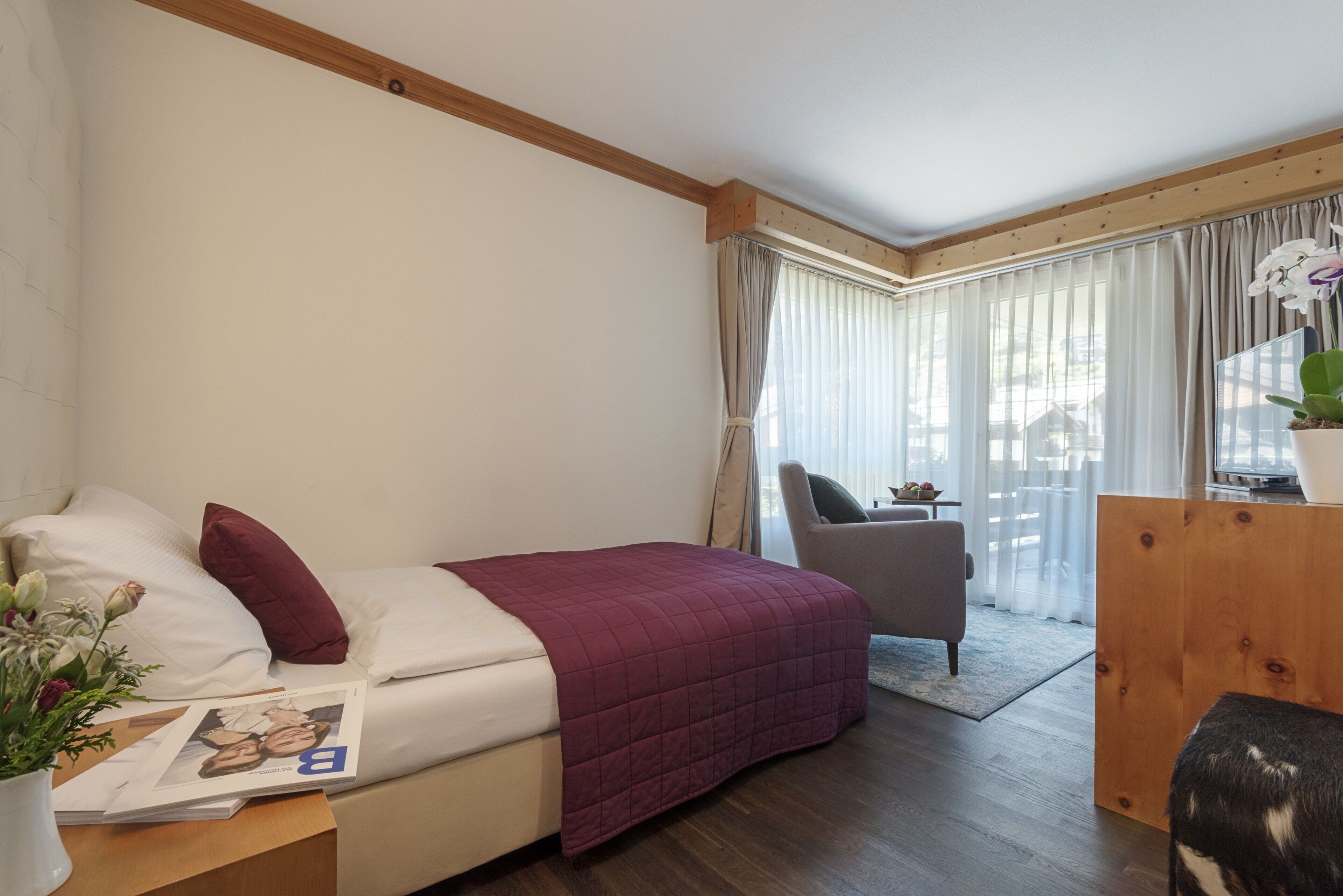A bedroom with a bed, a desk, a chair, and a window with curtains.