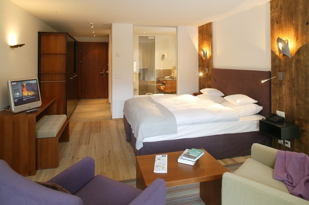 Une chambre d’hôtel avec un lit, un bureau, une chaise, une télévision et un mur en bois.