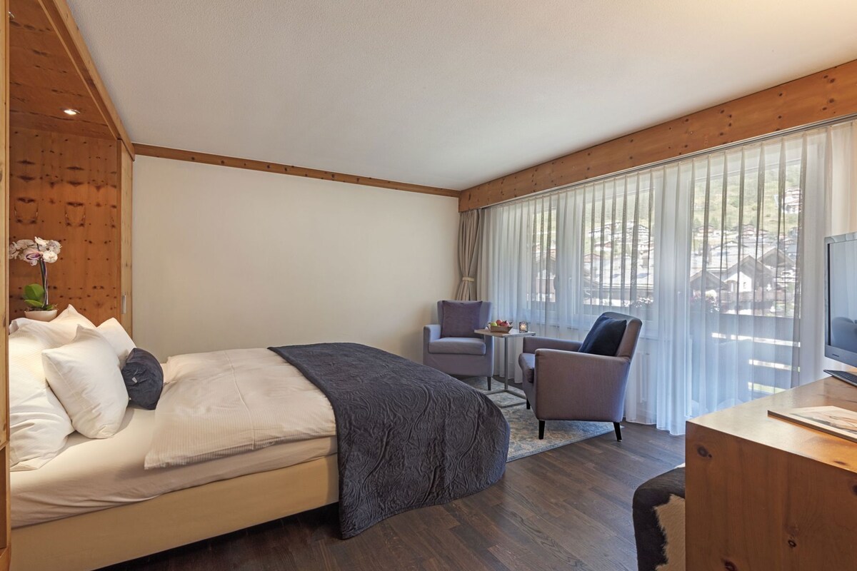 Un dormitorio con cama, escritorio, silla y ventana con cortinas.