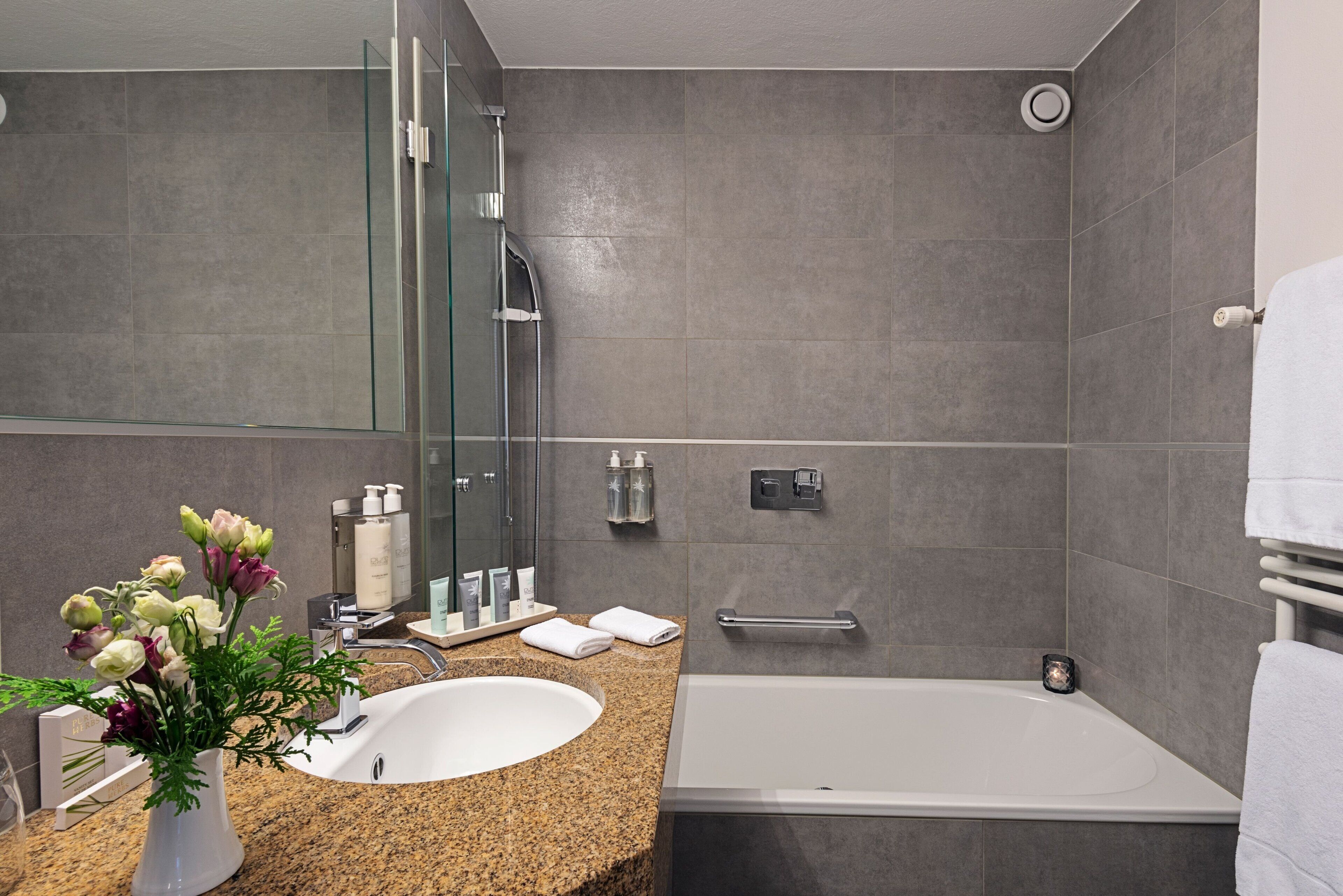 A modern bathroom with a granite countertop, a white sink, a glass shower enclosure, and a bathtub.