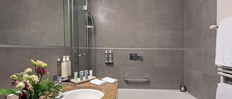 Une salle de bain moderne avec un comptoir en granit, un lavabo blanc, une douche en verre et une baignoire.