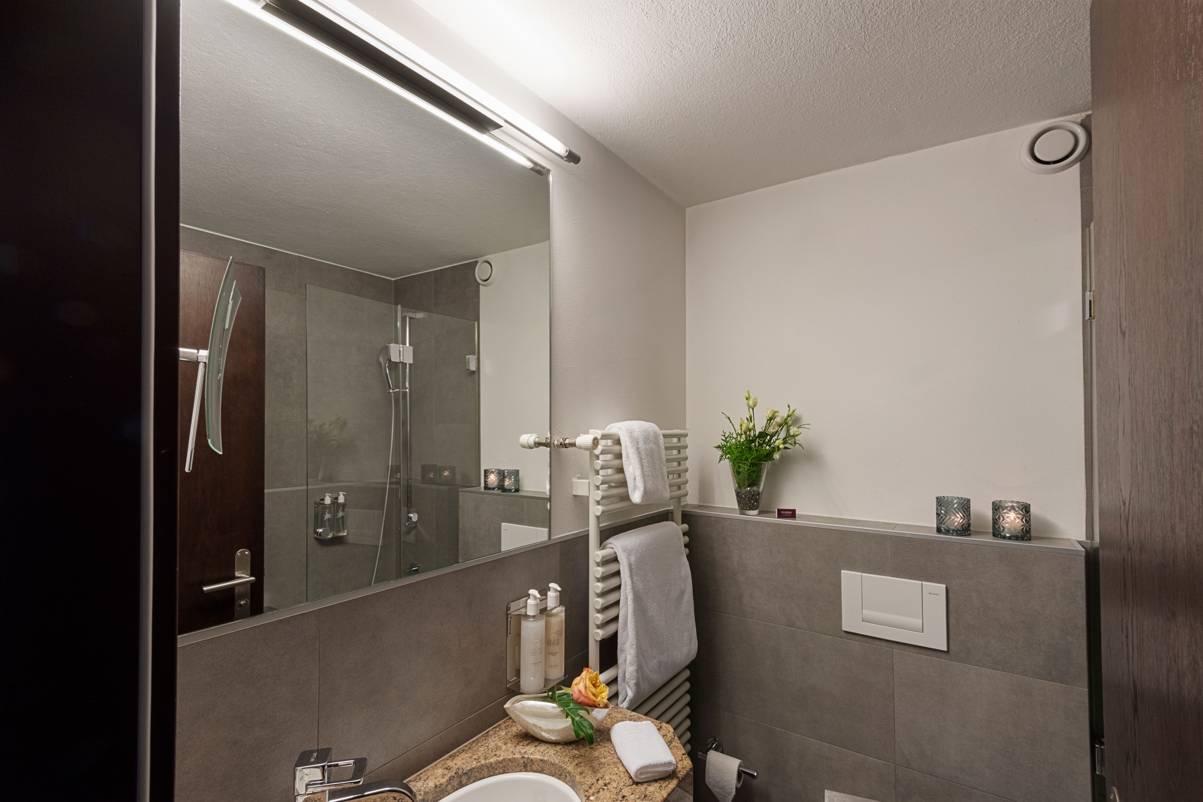 A modern bathroom with a glass shower, a sink with a granite countertop, and a mirror with a light above it.