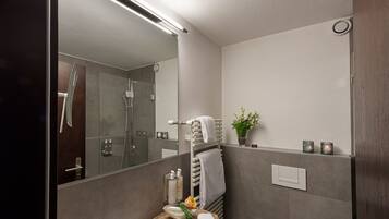 A modern bathroom with a glass shower, a sink with a granite countertop, and a mirror with a light above it.