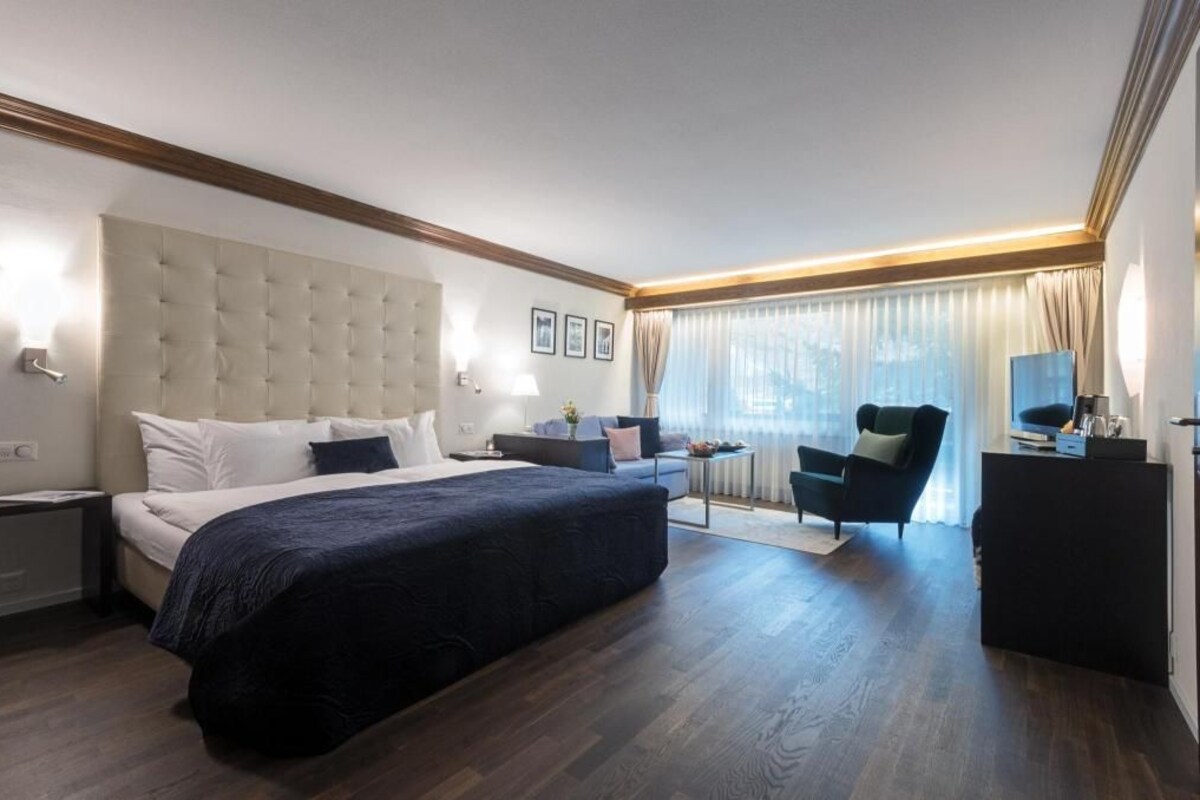 Habitación de hotel con una cama grande, un escritorio, una silla y una ventana con cortinas.