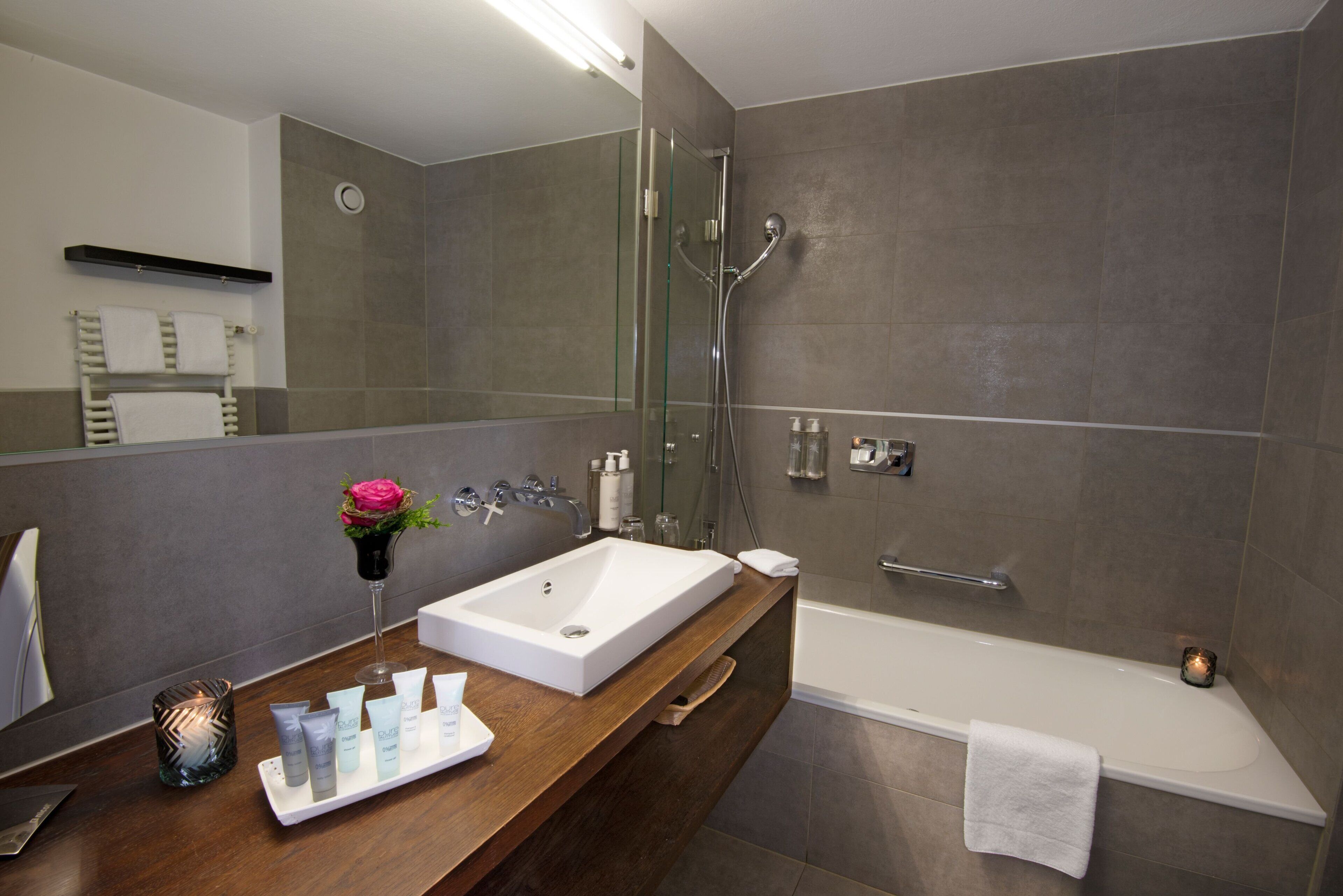 Un baño moderno con un espejo grande, un lavabo blanco, ducha con mampara de vidrio y una bañera.
