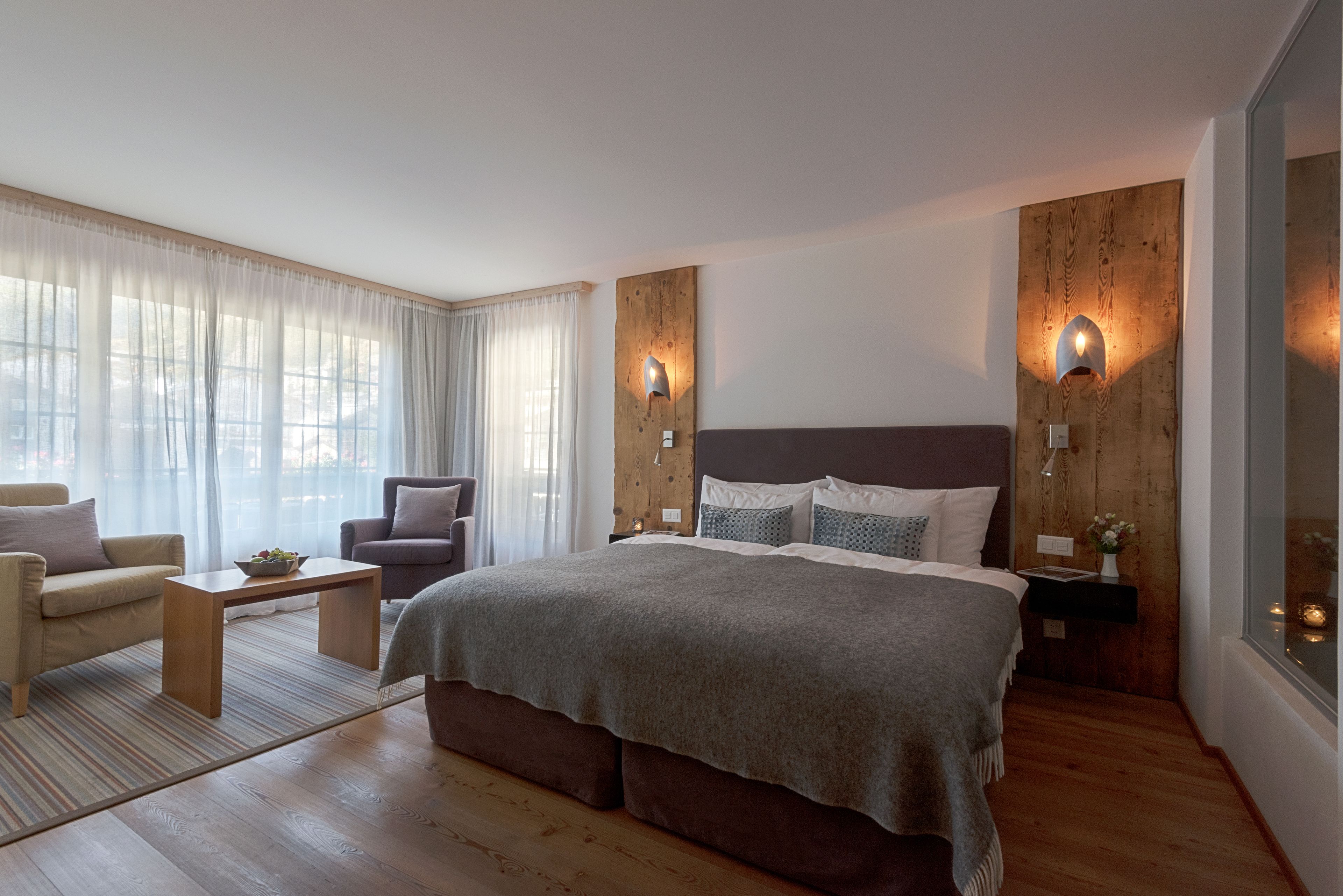 A modern bedroom with a large bed, two bedside tables, a nightstand, a sofa, and a chair.