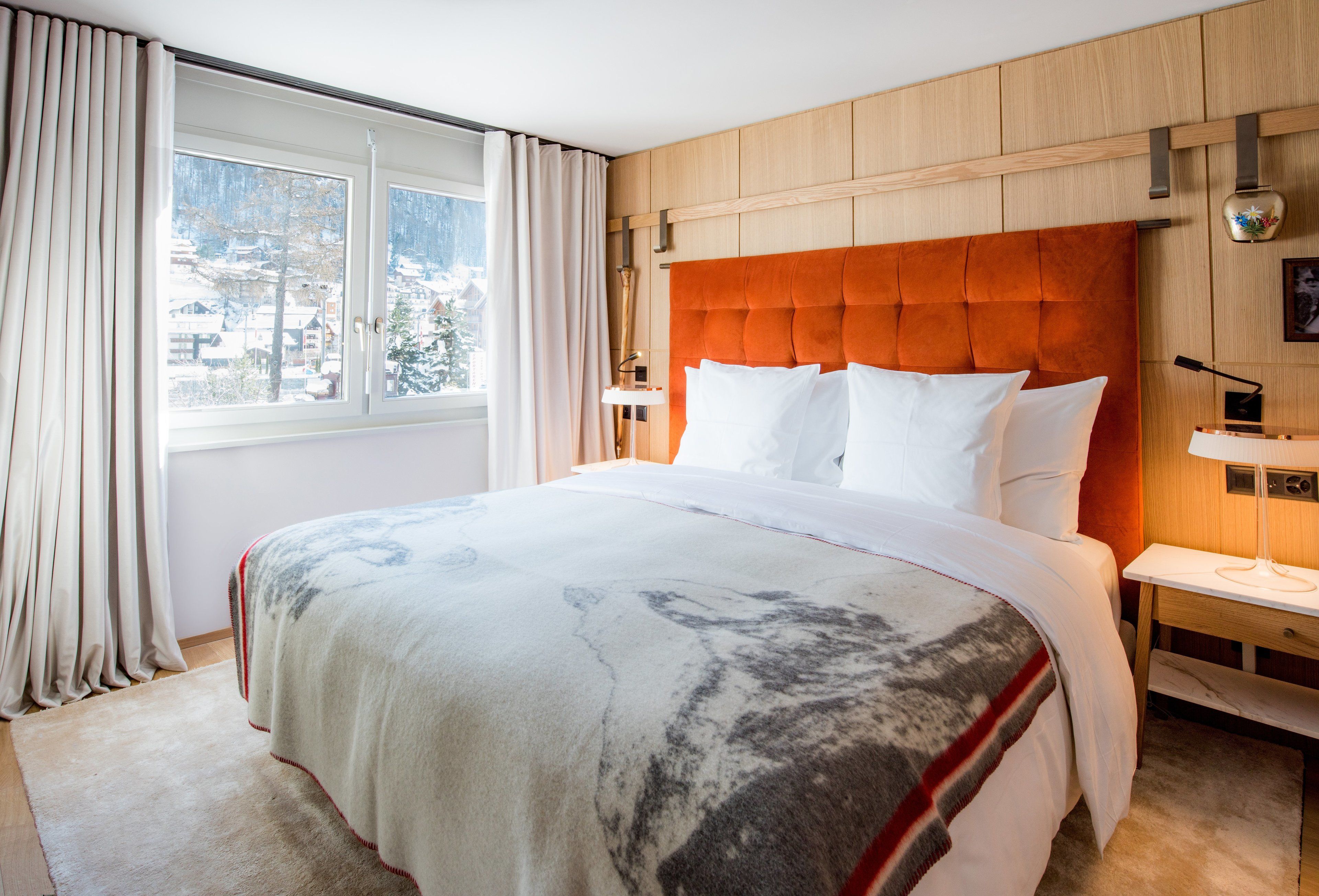 Habitación de hotel con una cama grande, cabecero de madera y vistas a un paisaje nevado a través de la ventana.