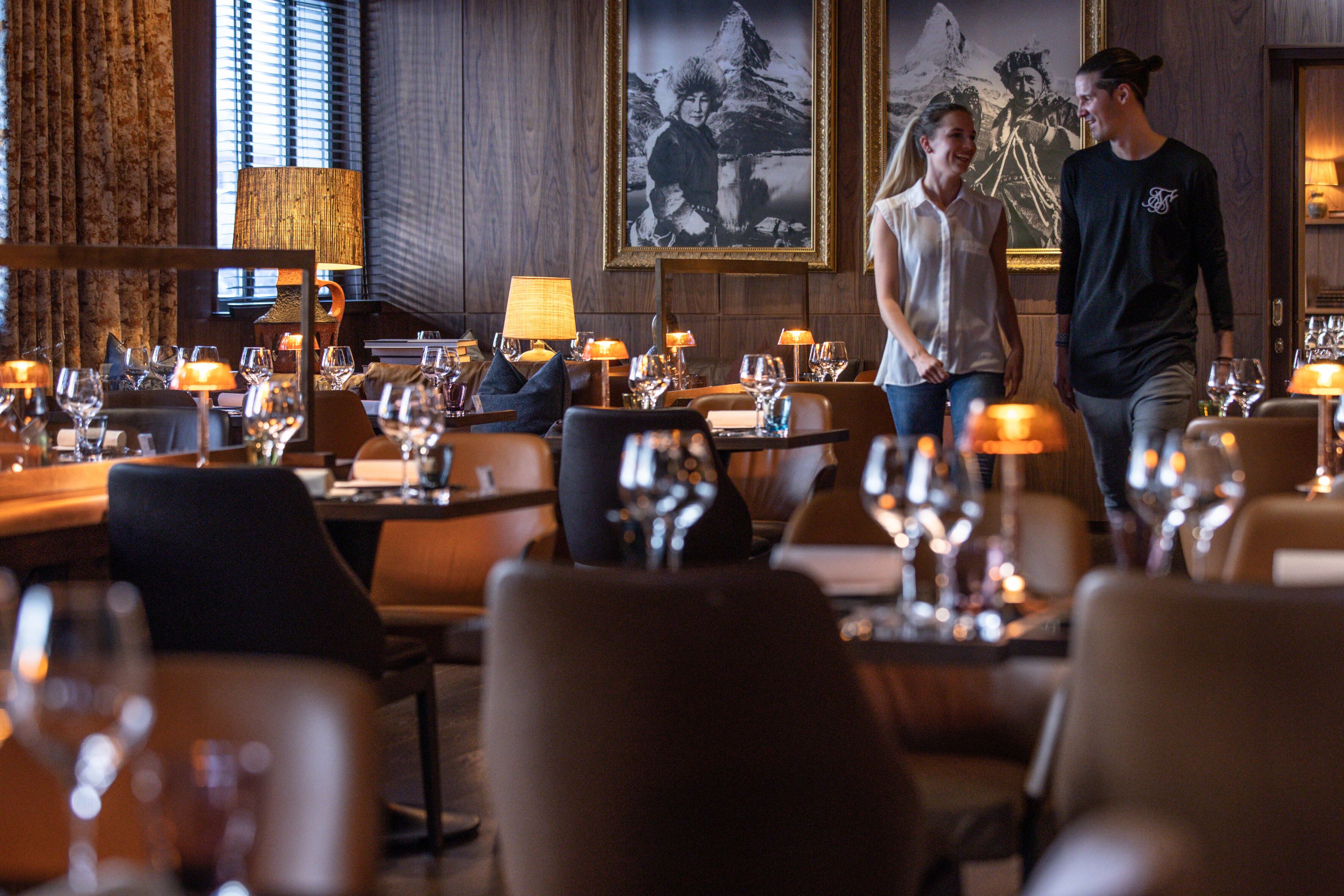 A restaurant interior with multiple dining tables, chairs, and a warm ambient lighting.