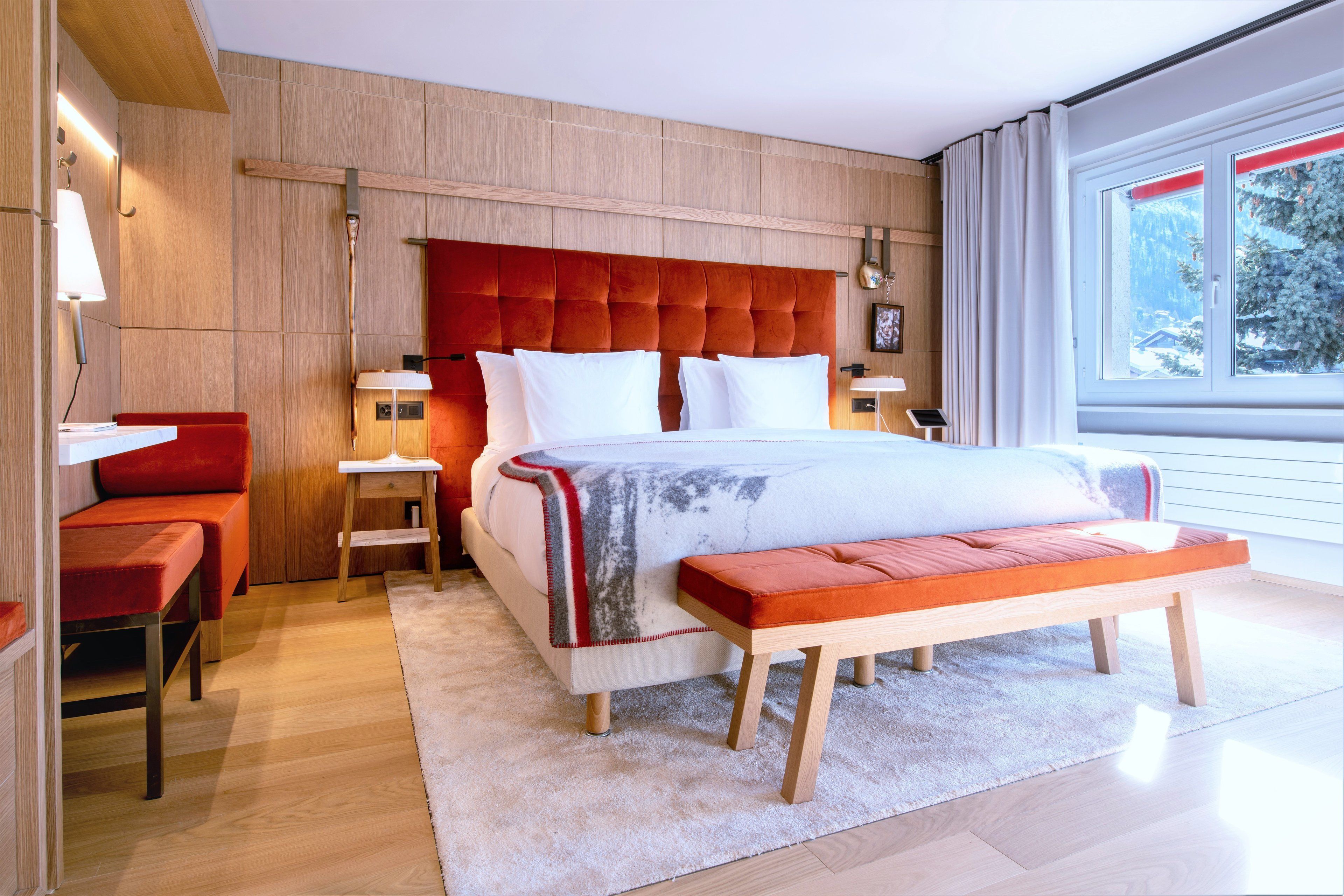 A modern bedroom with a large bed, a bench, a nightstand, and a red chair.
