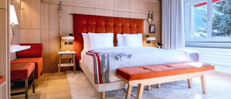 A modern bedroom with a large bed, a bench, a nightstand, and a red chair.