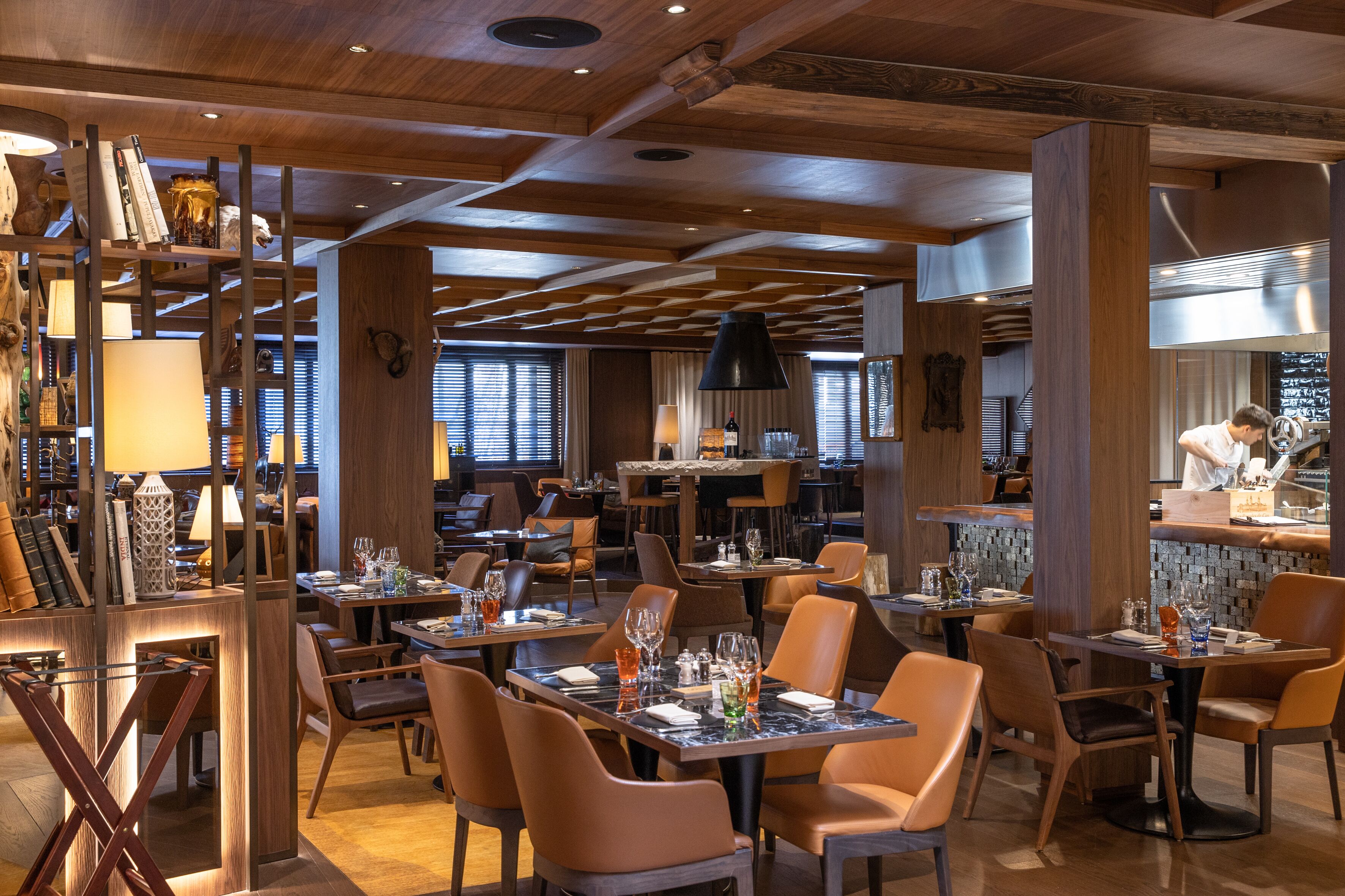 A restaurant interior with wooden beams, tables set for dining, and a bar area.