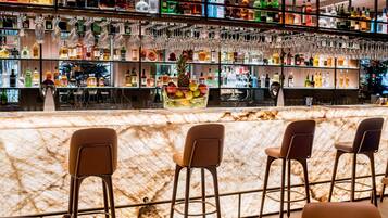Eine Bar mit Marmorplatte, mehreren Regalen voller Spirituosenflaschen und hängenden Gläsern.