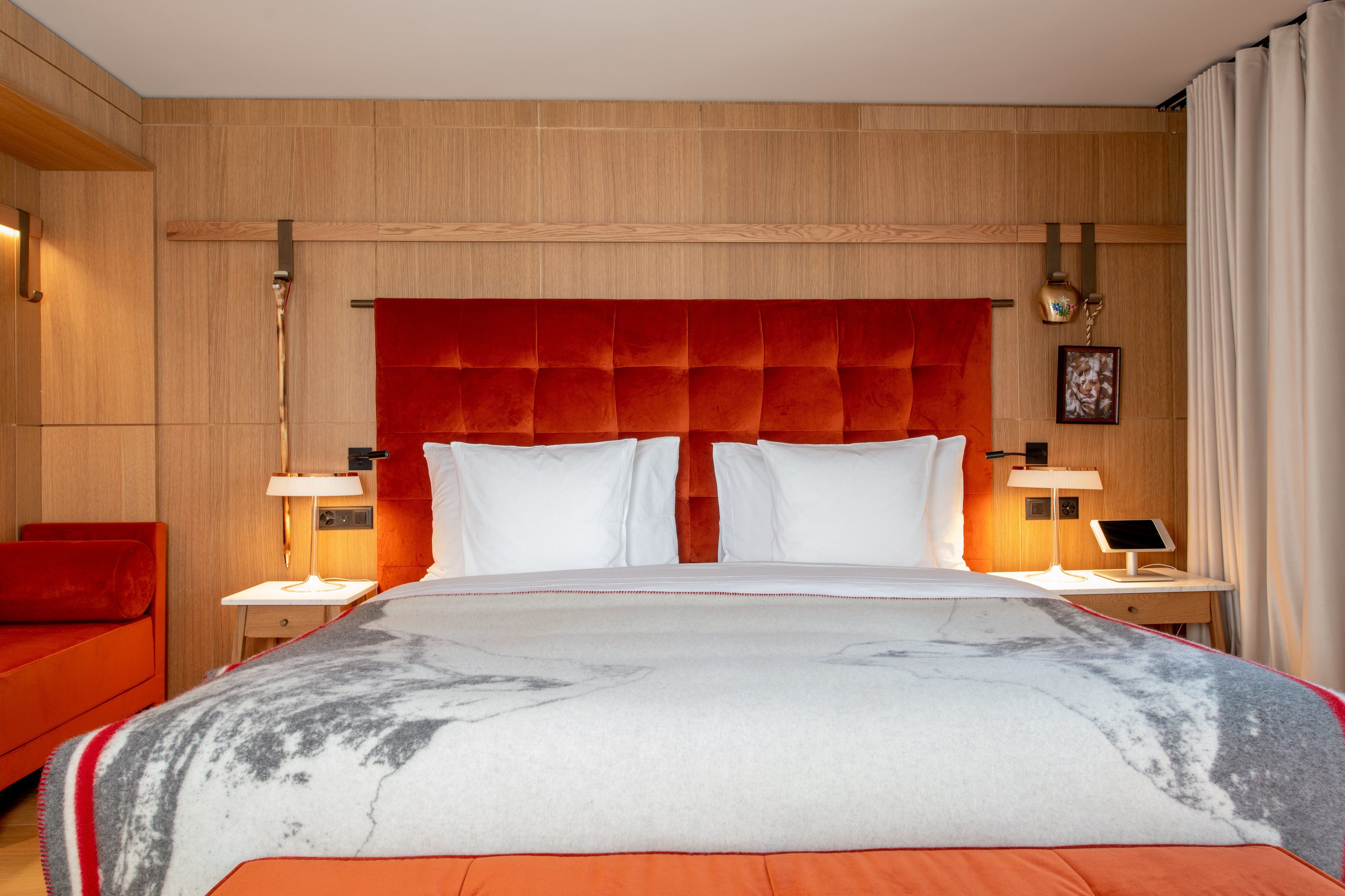 A hotel room with a large bed, two bedside tables with lamps, a red upholstered headboard, and a red sofa.