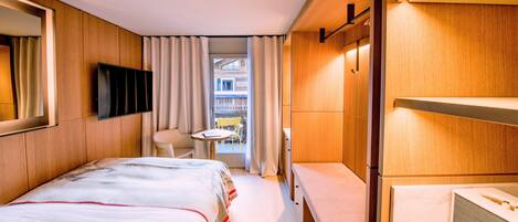A hotel room with a bed, a bedside table, a mirror, a TV, and a view of the outside balcony.