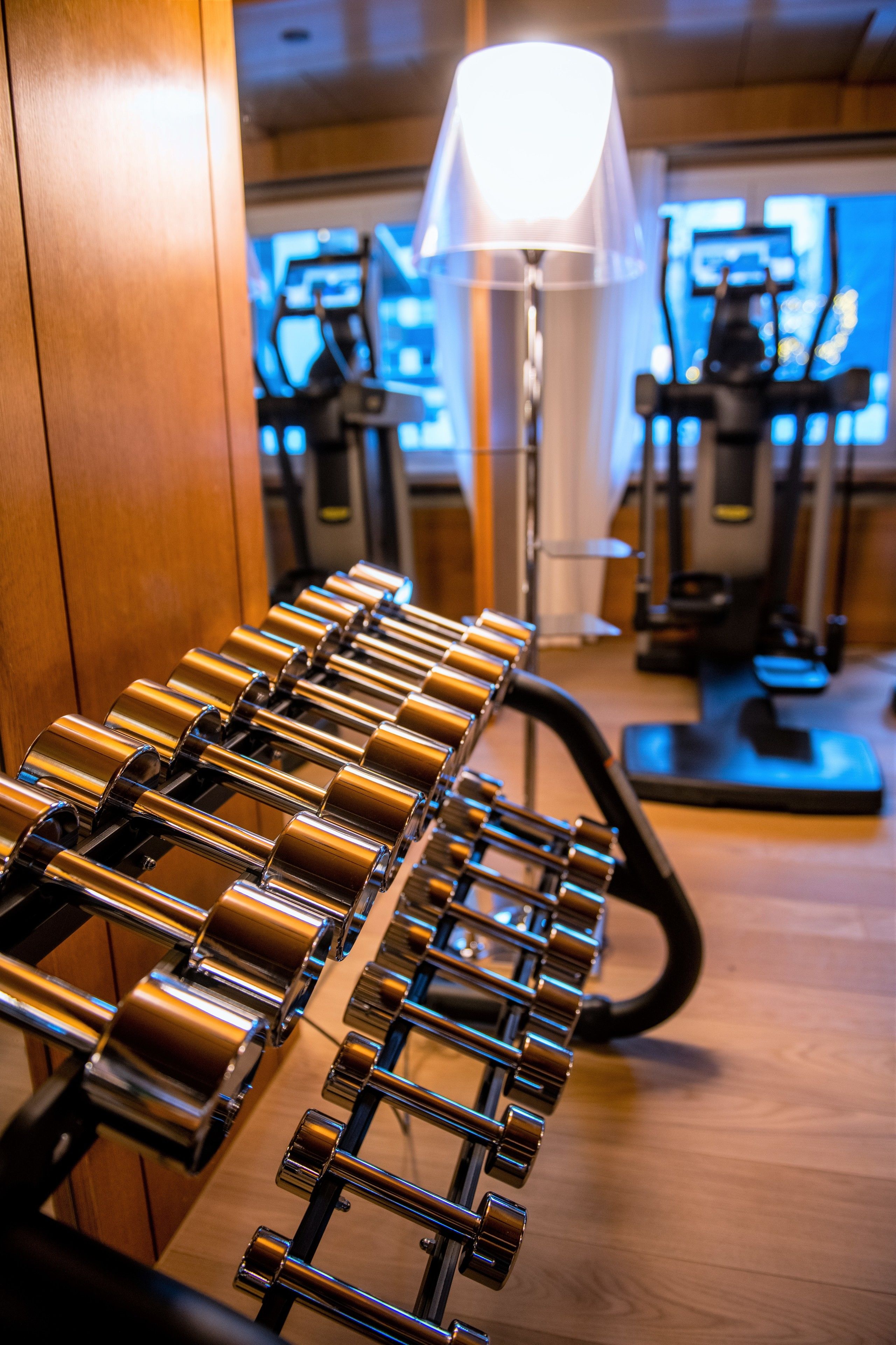 Ein Fitnessraum mit Trainingsgeräten, darunter eine Reihe von Kurzhanteln und Cardiogeräten.