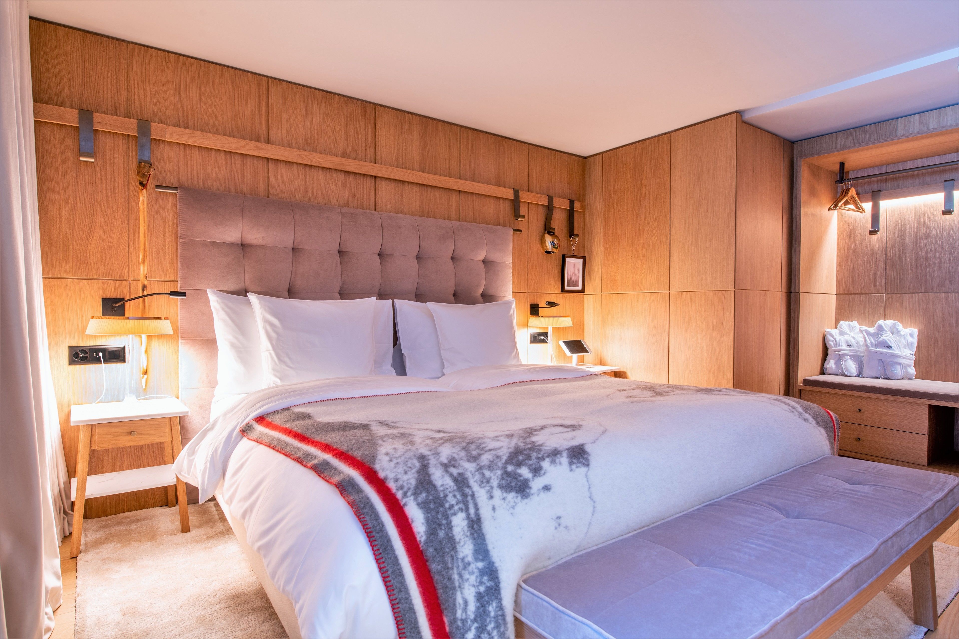 Een moderne slaapkamer met een groot bed, houten paneelwanden, een nachtkastje met een lamp en een klein plankje met handdoeken.