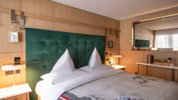 Una habitación de hotel con una cama grande, un cabecero de madera, mesitas de noche con lámparas, un espejo y un pequeño estante con libros y un vaso.